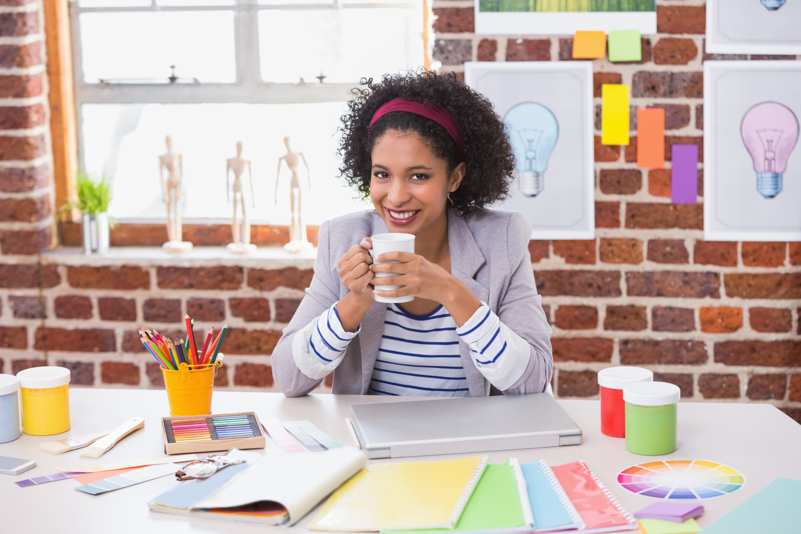 Portrait of smiling female interior designer with coffee cup sitting at office desk